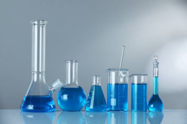 Aynanın yüzeyinde gri arka planda mavi sıvı bulunan laboratuvar camları. Metin için boşluk