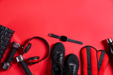Farklı spor aletleri, kol saati ve kırmızı arka planda kulaklıklar, düz yatış. Metin için boşluk