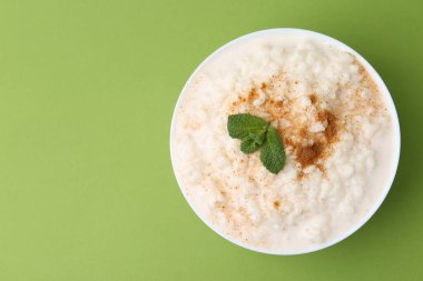 Tasty rice pudding with cinnamon and mint in bowl on green background, top view. Space for text