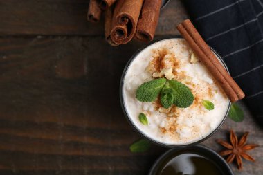 Tasty rice pudding with cinnamon, mint and nuts on wooden table, flat lay. Space for text