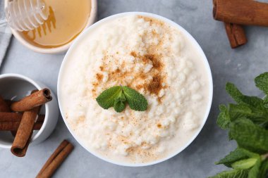 Tasty rice pudding with cinnamon, mint and honey on light grey table, flat lay