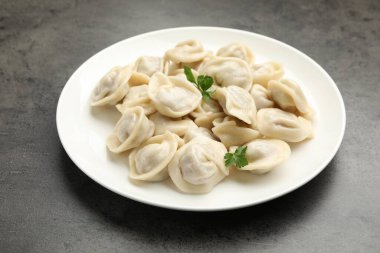 Delicious dumplings with fresh parsley on grey table, closeup
