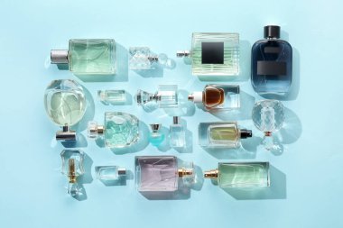 Bottles of various perfumes on light blue background, flat lay