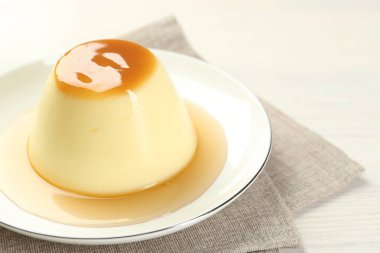 Delicious pudding with caramel sauce on white table, closeup. Space for text