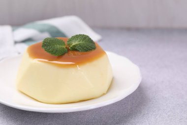 Delicious pudding with caramel sauce and mint on light table, closeup. Space for text