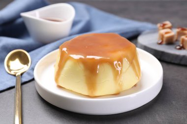 Delicious pudding with caramel sauce served on gray textured table, closeup