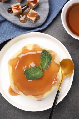 Delicious pudding with caramel sauce and mint served on gray textured table, flat lay