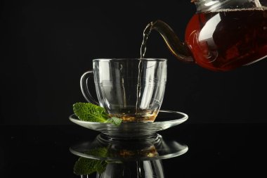 Koyu ayna masasında çaydanlıktan fincana taze demlenmiş çay dökülüyor.