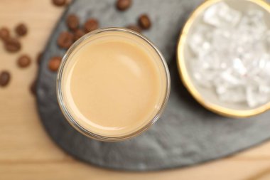 Coffee cream liqueur in glass, ice and beans on table, flat lay