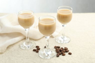 Coffee cream liqueur in glasses and beans on white textured table