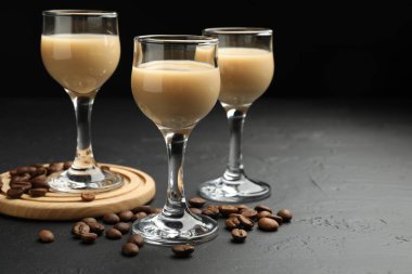 Coffee cream liqueur in glasses and beans on black table, space for text