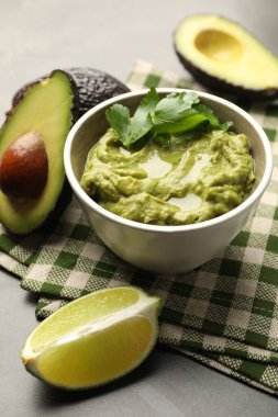 Lezzetli avokado sosu, maydanoz ve meyveler gri masada, yakın plan.