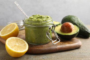 Tasty avocado dip in glass jar and fruits on wooden table, closeup