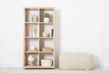 Shelving unit with different home decor and ottoman near white wall indoors