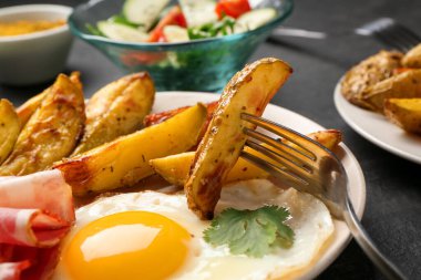 Tasty brunch. Fried egg, potato, bacon and fork on dark table, closeup