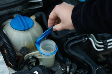 Arabanın ön cam temizleme deposunu açan adam, yakın plan.