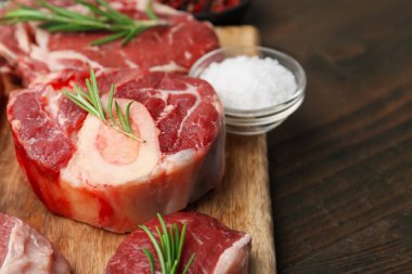 Pieces of raw beef, rosemary and salt on wooden table, closeup. Space for text