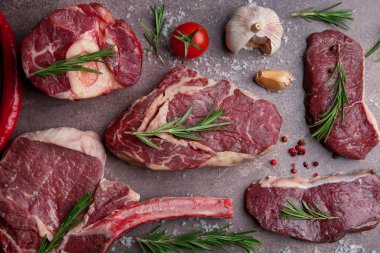 Flat lay composition with pieces of raw beef, salt, rosemary and products on brown textured table