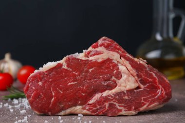 One piece of raw beef with salt on brown textured table against black background, closeup
