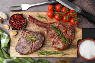Pieces of delicious beef meat, spices and tomatoes on brown table, top view