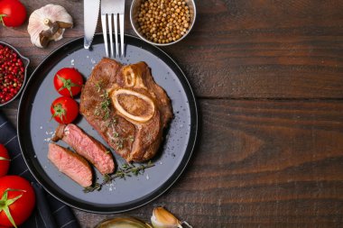 Pieces of delicious beef meat, spices and tomatoes on wooden table, flat lay. Space for text