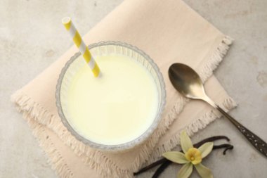 Glass of milk, vanilla pods, flower and spoon on light grey table, flat lay