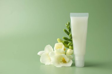 Açık yeşil arka planda dudak kremi ve frezya çiçekleri, yakın plan. Metin için boşluk