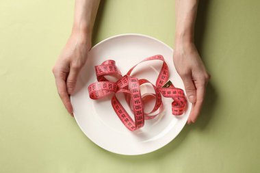 Bulimia. Yeşil arka planda mezurası olan kadın plakayı tutuyor.