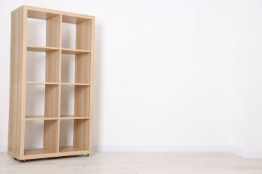 Empty wooden shelving unit near white wall indoors, space for text