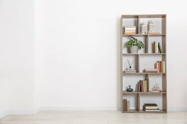 Wooden shelving unit with different home decor and houseplant near white wall indoors, space for text