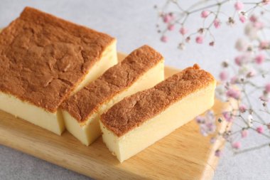 Tasty Japanese Castella sponge cake and flowers on light table, closeup