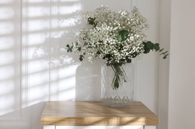 Beautiful gypsophila flowers and eucalyptus branches in vase on table at home