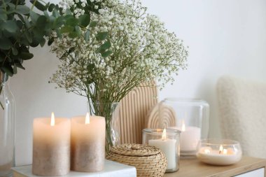 Beautiful gypsophila flowers, eucalyptus branches and burning candles on commode at home