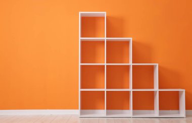 Empty shelving unit near orange wall indoors. Space for text