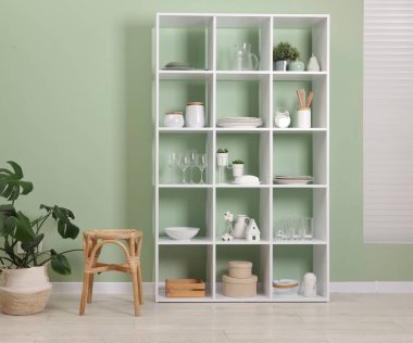 Shelving unit with dishware near olive wall indoors