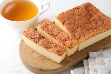 Cut tasty Japanese Castella sponge cake and tea on white wooden table, closeup