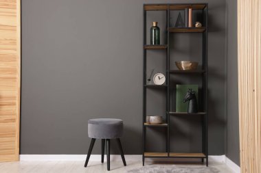 Shelving unit with decor, stool and folding screen near grey wall indoors