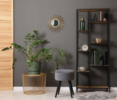 Shelving unit with decor, stool and folding screen near grey wall indoors