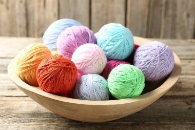 Balls of colorful yarn in bowl on wooden table, closeup