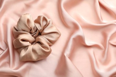 Hair scrunchie on pink silk fabric, top view. Space for text
