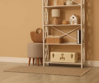 Shelving unit with decor, stool and wicker bag near beige wall indoors