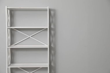 Empty shelving unit near light grey wall. Space for text
