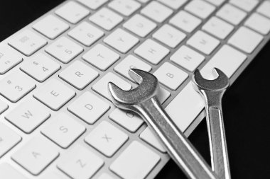 Technical support concept. Wrenches and keyboard on black background, closeup