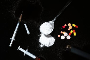 Drug addiction. Spoon with powder, pills and cigarette lighter on black table, flat lay