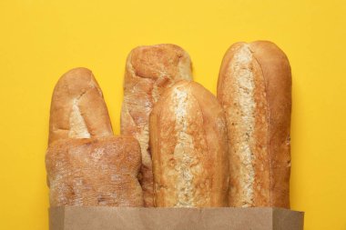 Sarı arka planda taze baget ve ciabatta ile kağıt torba, üst manzara