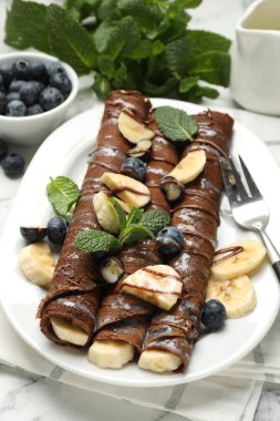 Beyaz mermer masada servis edilen muzlu ve yaban mersinli leziz çikolatalı krepler.