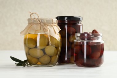 Pickled olives in glass jars on white wooden table