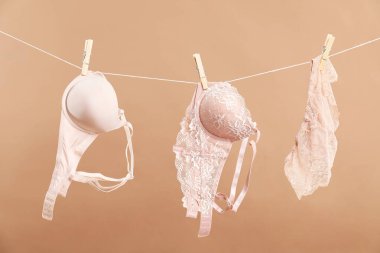 Beautiful bras and panties hanging on rope against dark beige background