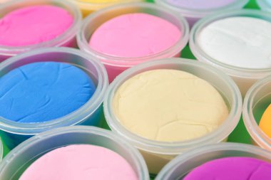 Different colorful modeling clay in plastic jars on green background, closeup