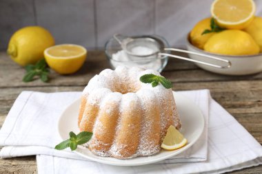 Pudra şekerli lezzetli limonlu pasta, taze meyve dilimi ve ahşap masada nane.